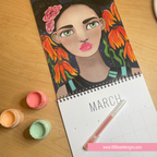 A spiral-bound March calendar lies open on a wooden table, featuring a colorful painted portrait of a woman with flowers in her hair. Paintbrushes and small paint pots are placed beside it, and a pink website watermark appears at the bottom.
