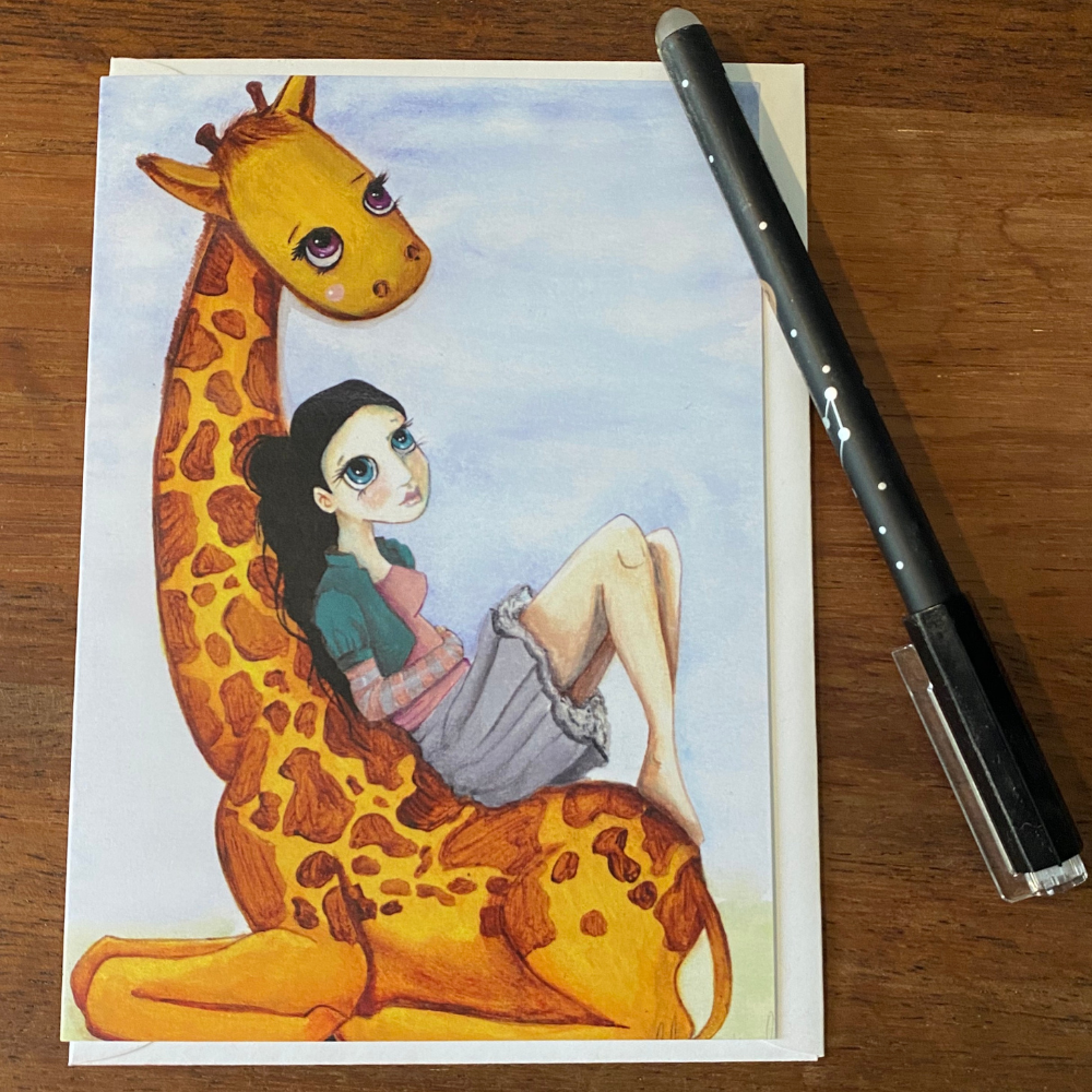 Illustration of a girl sitting on a giraffe with a pen next to it on a wooden surface GREETING CARD