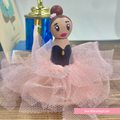 A hand-painted wooden peg doll styled as a ballerina, featuring a pink dress, black tulle skirt, and brown hair in a bun, displayed on a wooden surface.