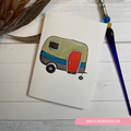 Colorful drawing of a camper on a piece of paper with a pen and plant in the background.  GREETING CARD