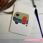 Colorful drawing of a camper on a piece of paper with a pen and plant in the background.  GREETING CARD
