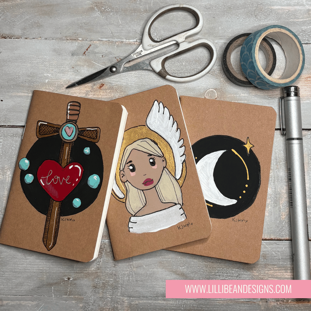 Three decorated notebooks with artistic designs on a wooden surface with scissors and tape.