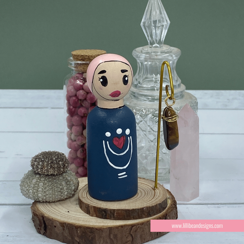 Peg doll with a heart design on a wooden stand with decorative items in the background.