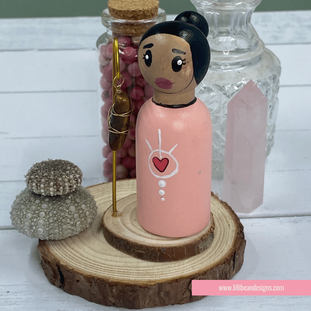 Peg doll with pink dress and heart design on a wooden stand, with jars in the background.