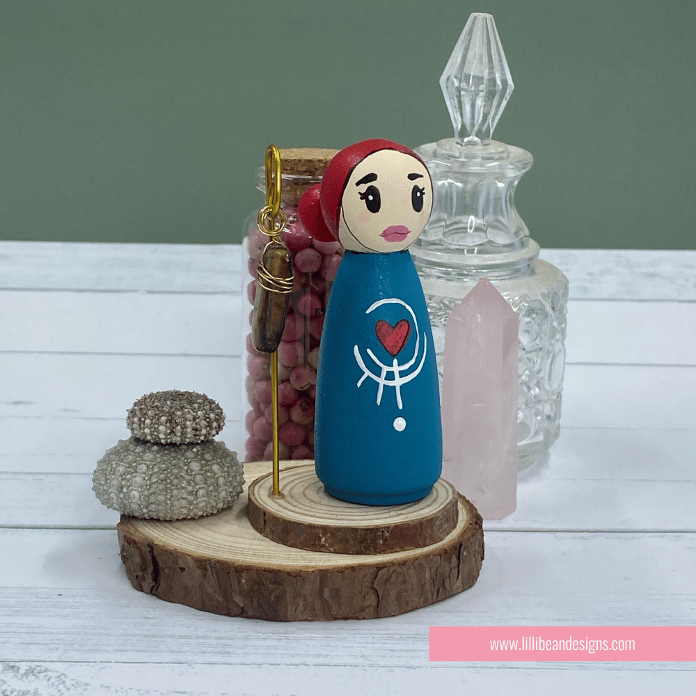 Decorative figurine with a blue dress and red headscarf on a wooden base with a green background.