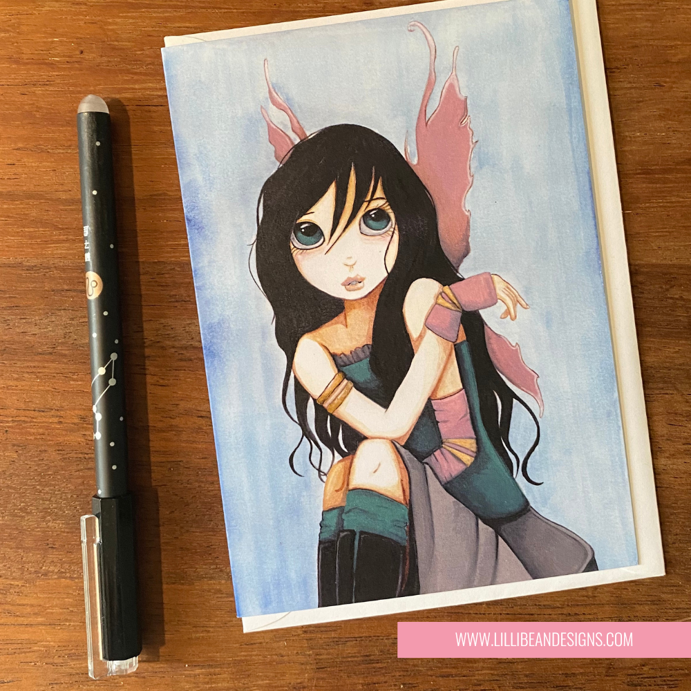 Illustration of a fantasy character on a GREETING CARD with a pen next to it on a wooden surface.