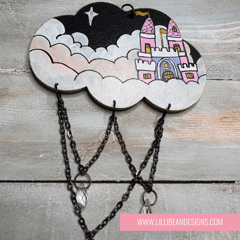 Decorative cloud-shaped hooks with illustrations on a wooden surface, labeled with castle image. LilliBean Designs