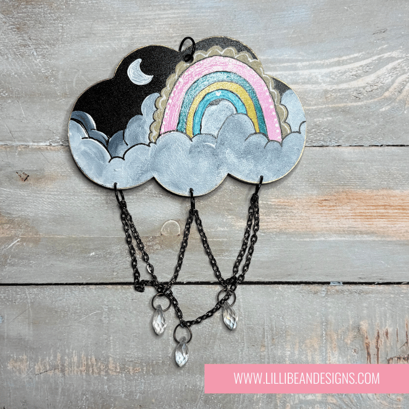 Decorative cloud-shaped hooks with illustrations on a wooden surface, labeled with rainbow image. LilliBean Designs
