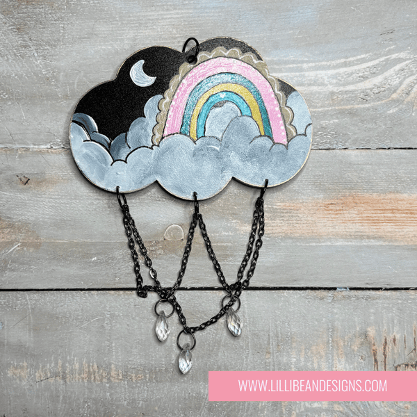 Decorative cloud-shaped hooks with illustrations on a wooden surface, labeled with rainbow image. LilliBean Designs