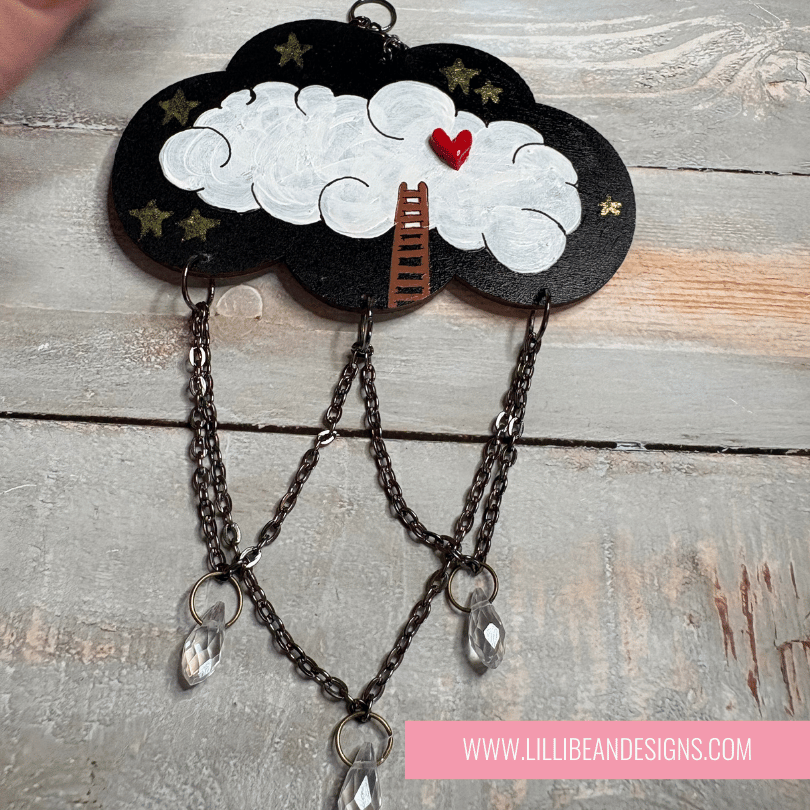 Decorative cloud-shaped hooks with illustrations on a wooden surface, labeled with ladder to cloud image. LilliBean Designs