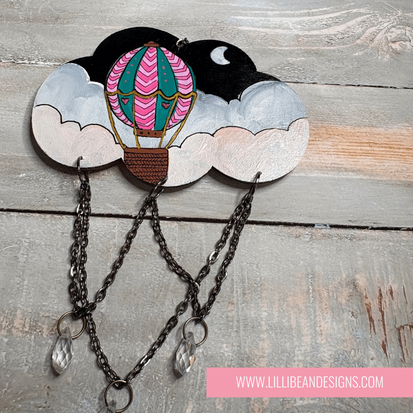 Decorative cloud-shaped hooks with illustrations on a wooden surface, labeled with hot air balloon image. LilliBean Designs
