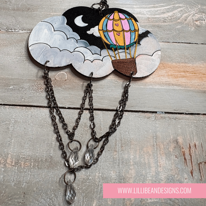 Decorative cloud-shaped hooks with illustrations on a wooden surface, labeled with hot air balloon image. LilliBean Designs