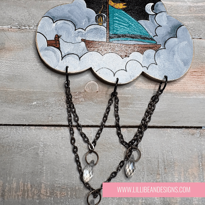 Decorative cloud-shaped hooks with illustrations on a wooden surface, labeled with sailing boat image. LilliBean Designs