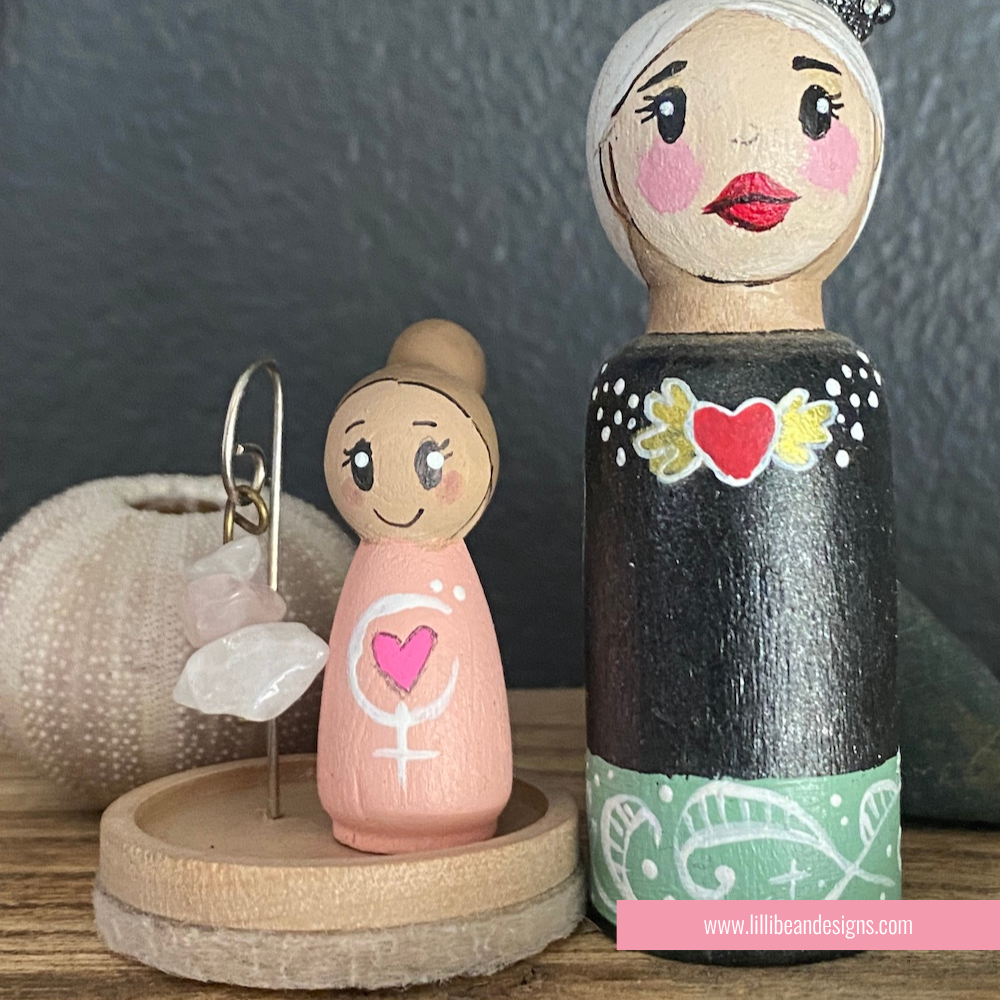 Two wooden peg dolls with decorative elements on a dark background
