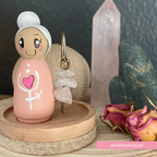 Small figurine with a heart design on a wooden stand, surrounded by crystals and flowers.