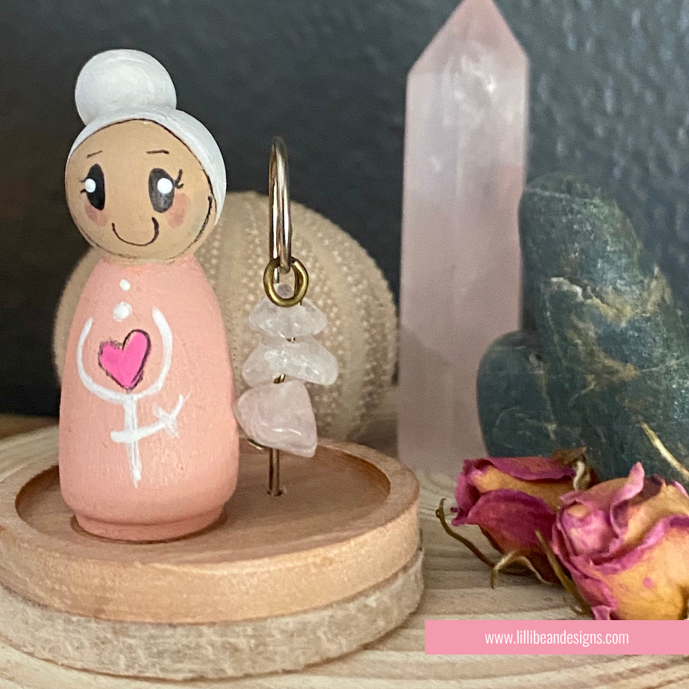 Small figurine with a heart design on a wooden stand, surrounded by crystals and flowers.