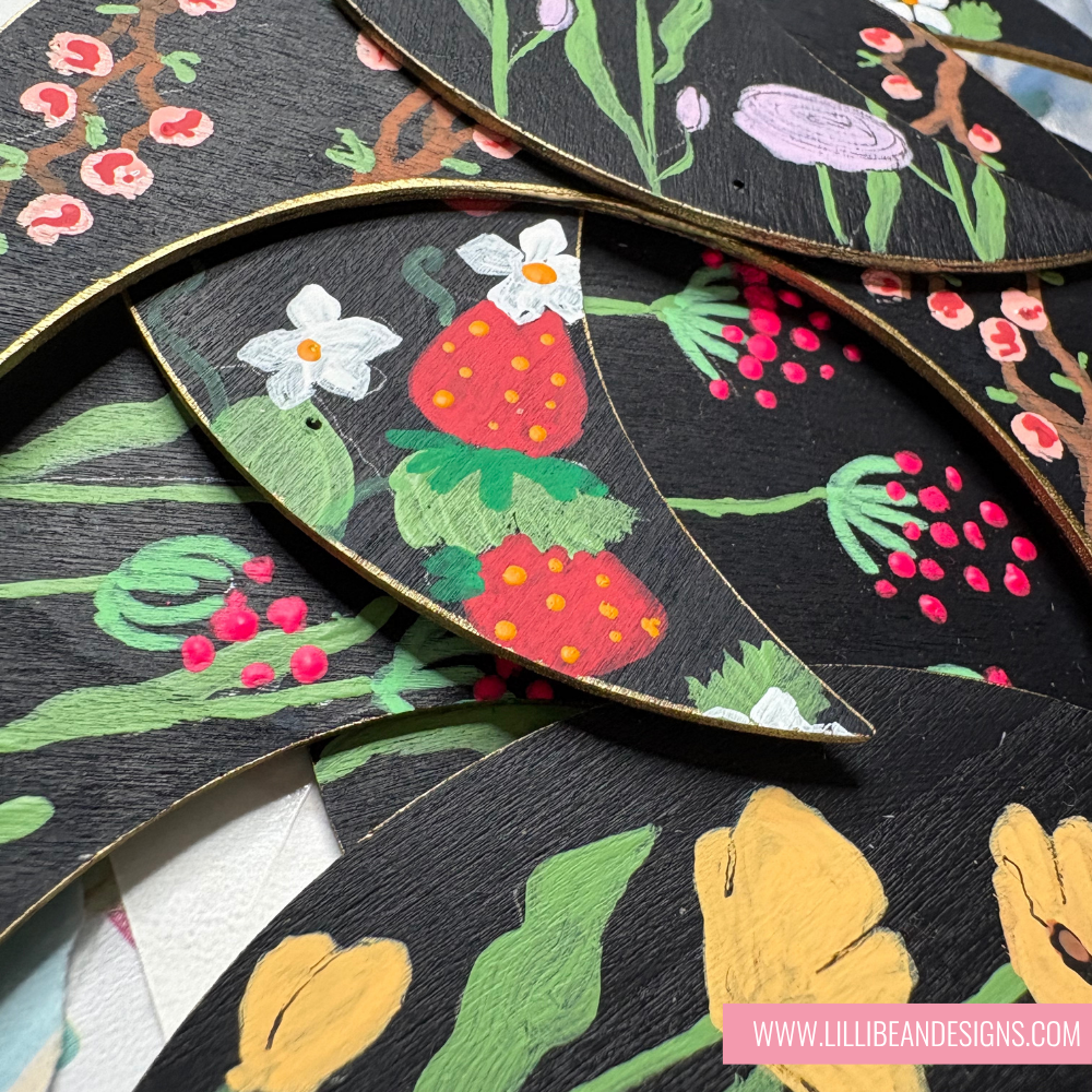 Decorative wooden leaves with floral and strawberry designs on a black background. LilliBean Designs