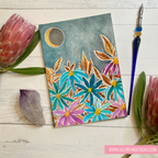 Colorful floral card with moon and stars on a wooden surface with flowers and tools.