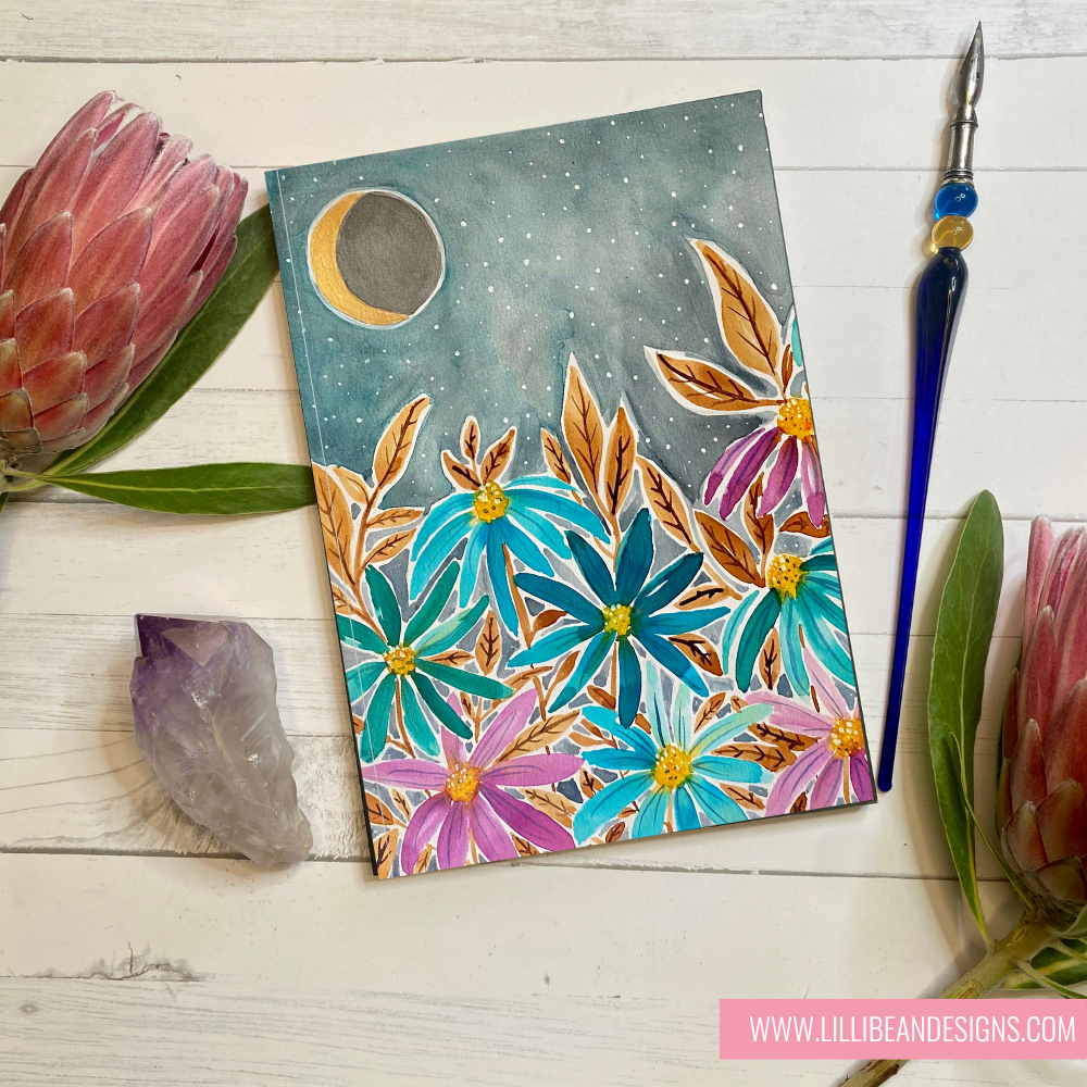 Colorful floral card with moon and stars on a wooden surface with flowers and tools.