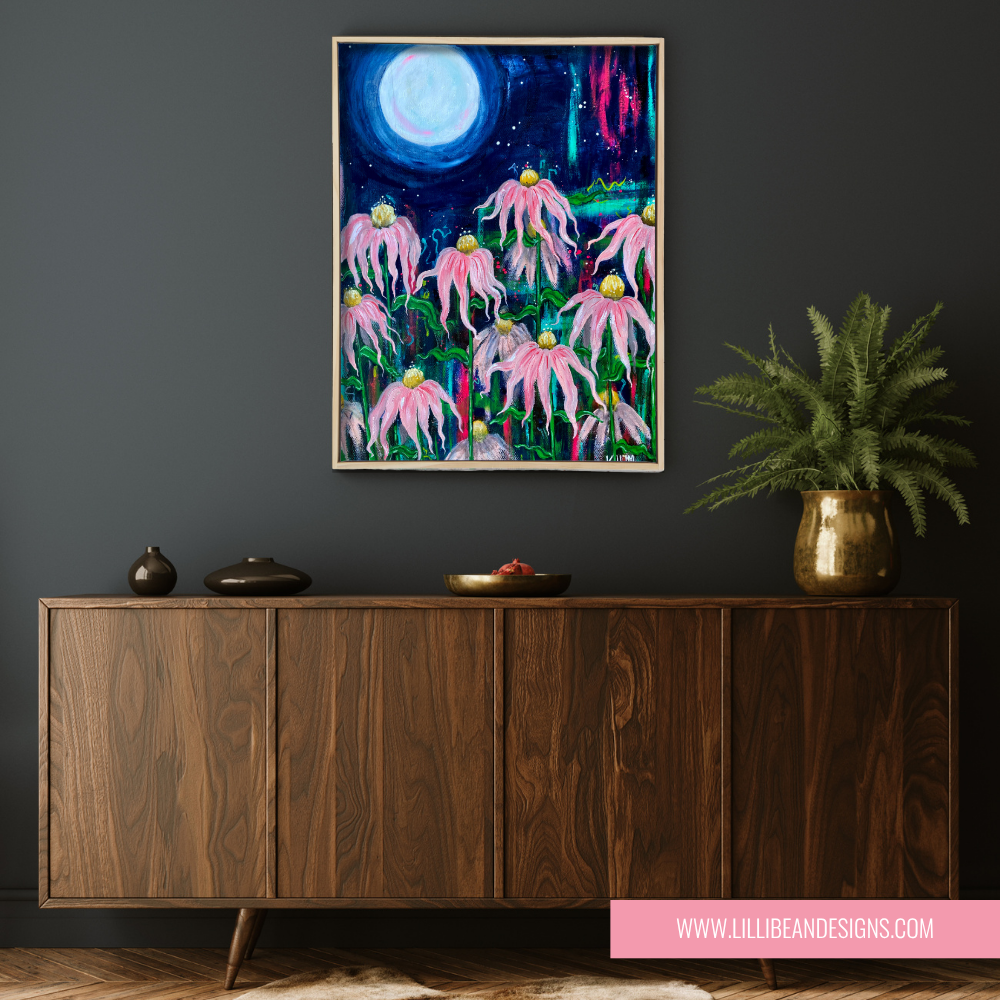 Framed artwork of pink echinacea flowers with a moonlit sky above a wooden cabinet.
