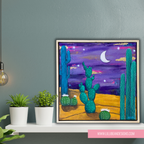 Framed artwork of a desert scene with cacti on a shelf against a gray wall.