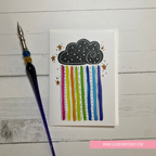 Card with a cloud and rainbow design on a wooden surface with a pen.