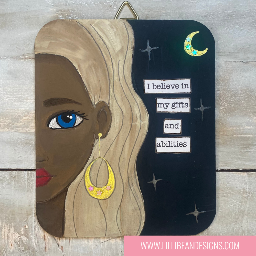 Decorative wall art with a woman's face, earrings, and motivational quote on a wooden background.