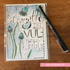 Handmade card with motivational quote 'Strength in Vulnerability' on a wooden surface with a pen.