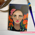 Artistic depiction of a woman with flowers in her hair on a wooden surface with a pen and plant. GREETING CARD