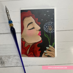 Artistic depiction of a woman holding a dandelion with a paintbrush on a wooden surface, featuring LillieBean Designs branding. GREETING CARD