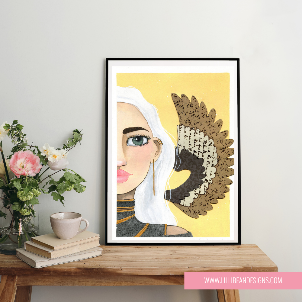 Framed artwork of a stylized face with a yellow background on a wooden table with books and flowers.