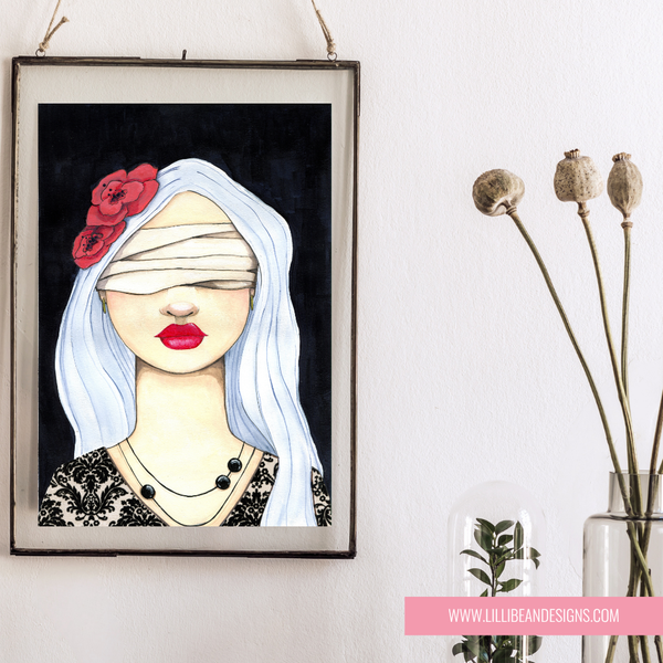 A framed art print featuring a stylized illustration of a blindfolded woman with white hair, red lips, and a red flower on her head, hanging on a white wall next to dried flowers in a glass vase.