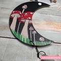 Decorative moon-shaped ornament with painted mushrooms on a wooden surface.