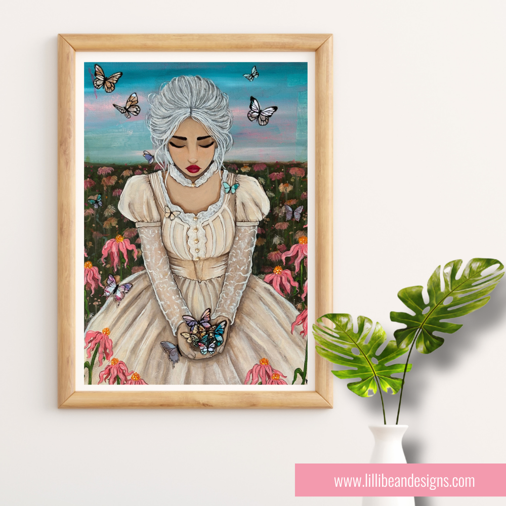 A framed art print featuring a stylized illustration of a woman with white hair in a cream dress, surrounded by pink flowers and butterflies, displayed on a light wall next to a green plant in a white vase.