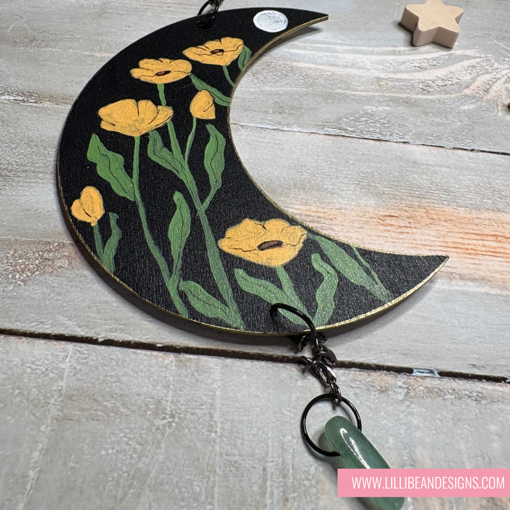 Decorative keychain with floral design on a crescent moon shape, featuring yellow flowers and green leaves.