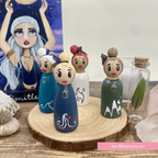 Set of wooden peg dolls with unique designs on a wooden stand, with a blurred background.