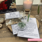 Herbal mixture in a small glass jar with instructions on a wooden surface, surrounded by candles and packaging.