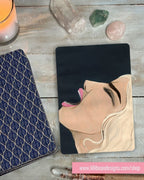 Black background, face in a scream with a design of a woman's face on a wooden surface with decorative items.