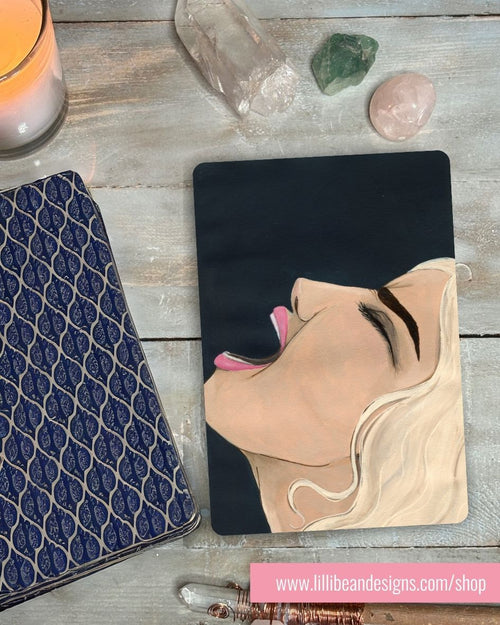 Black background, face in a scream with a design of a woman's face on a wooden surface with decorative items.