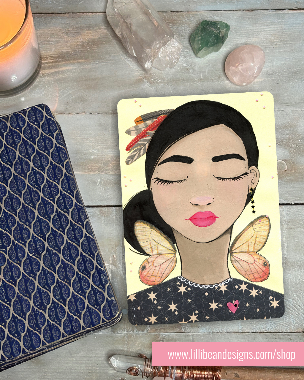 Card with a stylized illustration of a woman with butterfly wings on a wooden surface with crystals and a candle.