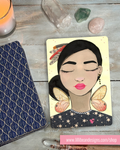 Card with a stylized illustration of a woman with butterfly wings on a wooden surface with crystals and a candle.