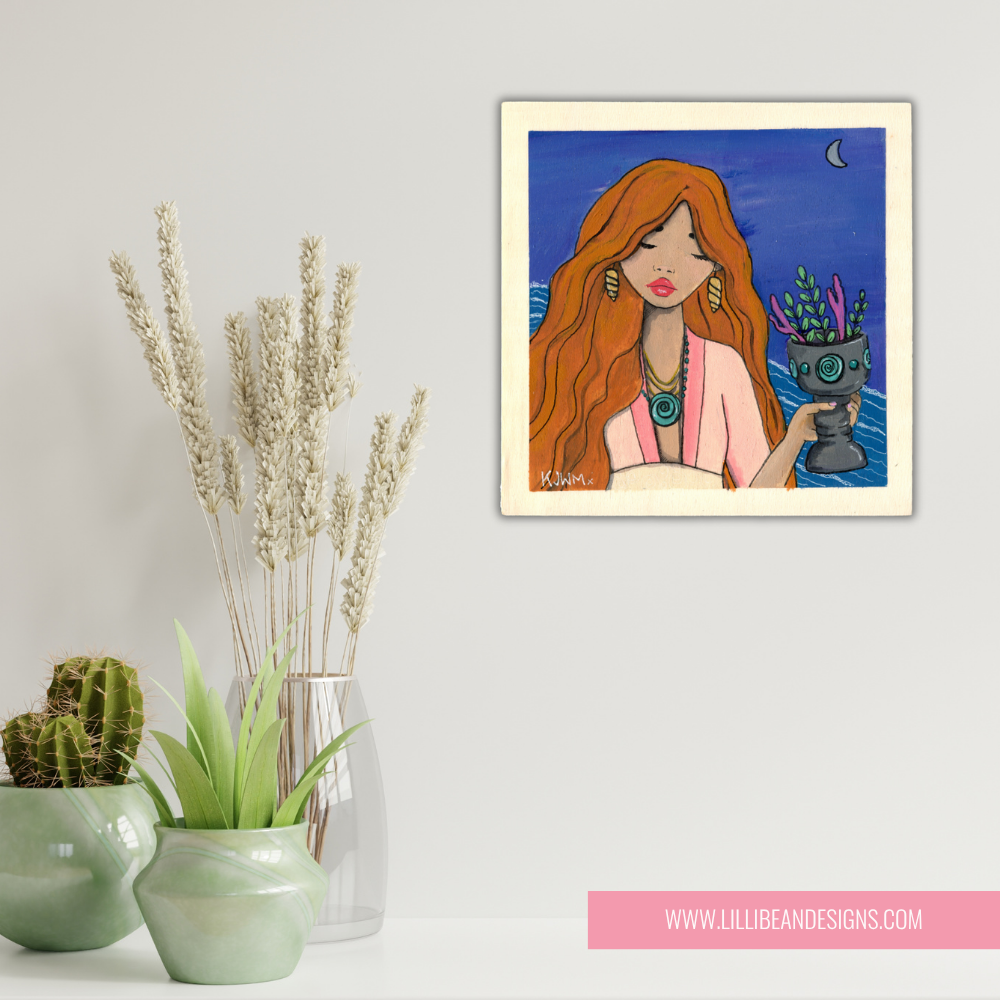 Framed artwork of a woman with red hair holding a plant, displayed on a wall with decorative plants below.