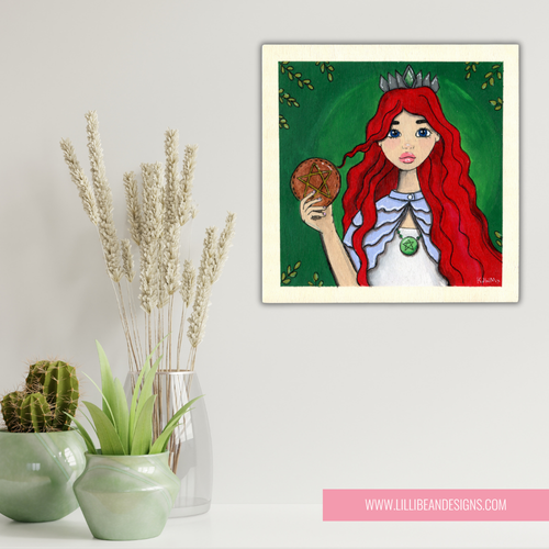 Framed artwork of a red-haired woman with a crown holding a fruit, placed on a surface with decorative plants.