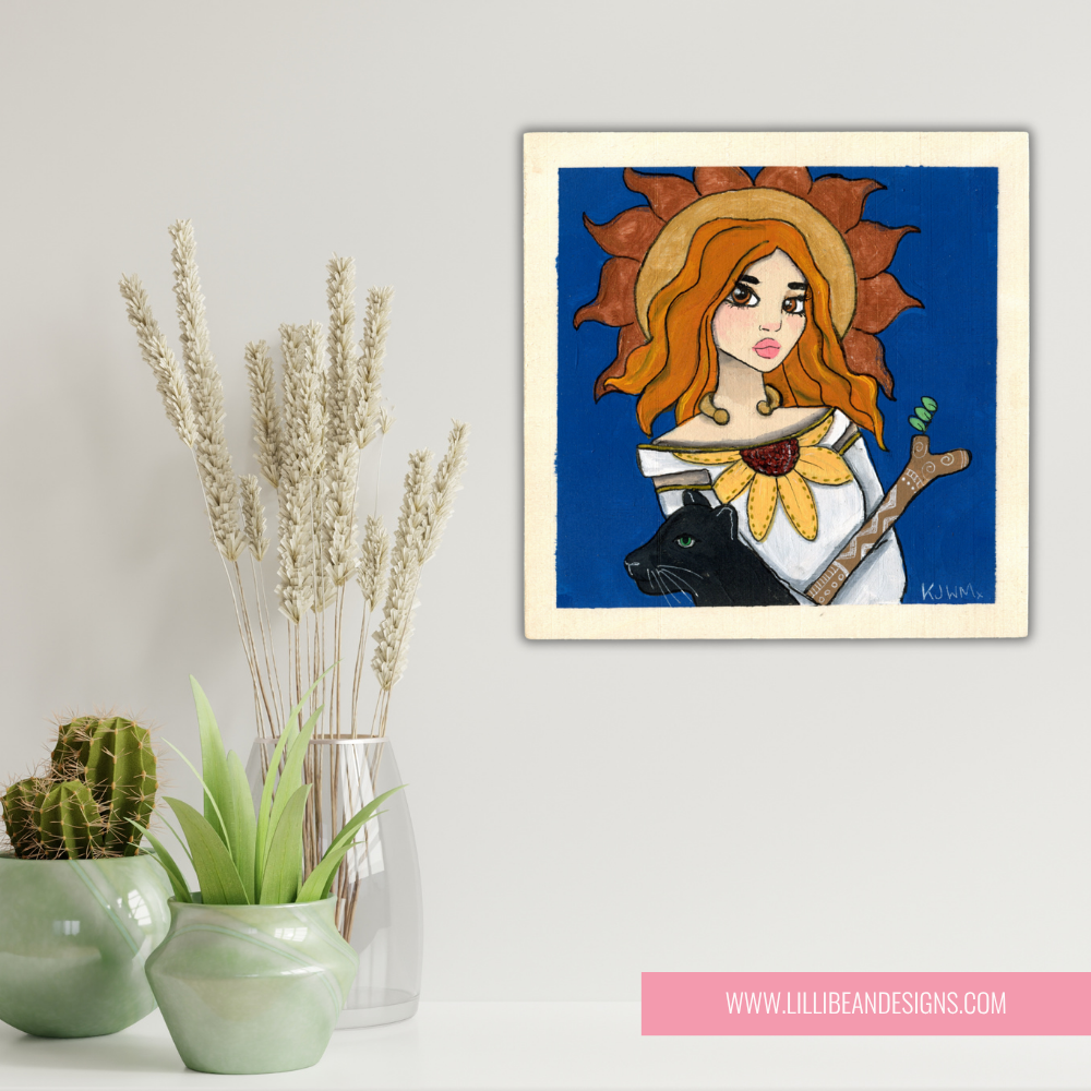 Framed artwork of a woman with sunflower hair and a black cat, displayed on a wall with decorative plants.