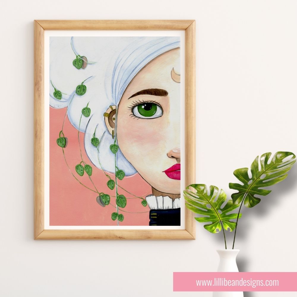 Framed artwork of a woman's face with green leaves on a white wall.