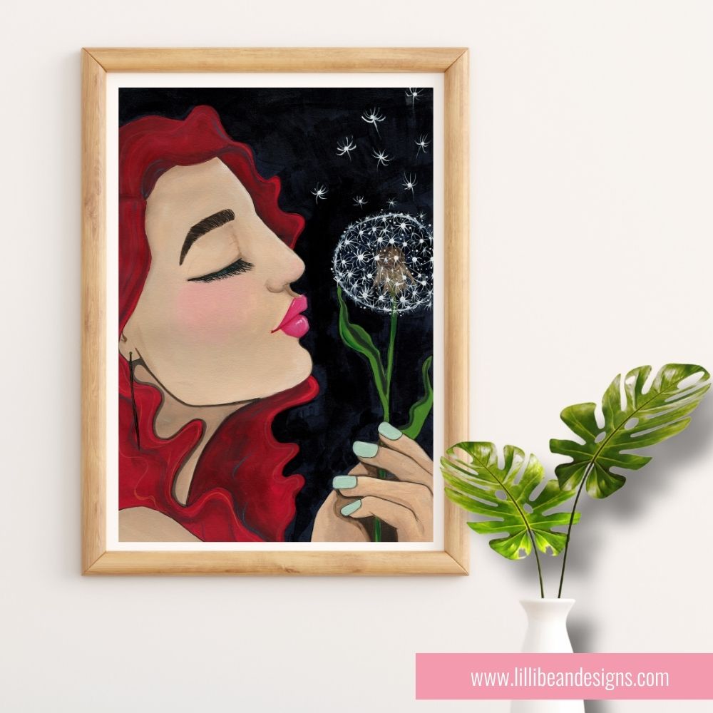 Framed artwork of a woman blowing on a dandelion with a wooden frame, placed on a white surface.