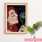 Framed artwork of a woman blowing on a dandelion with a wooden frame, placed on a white surface.