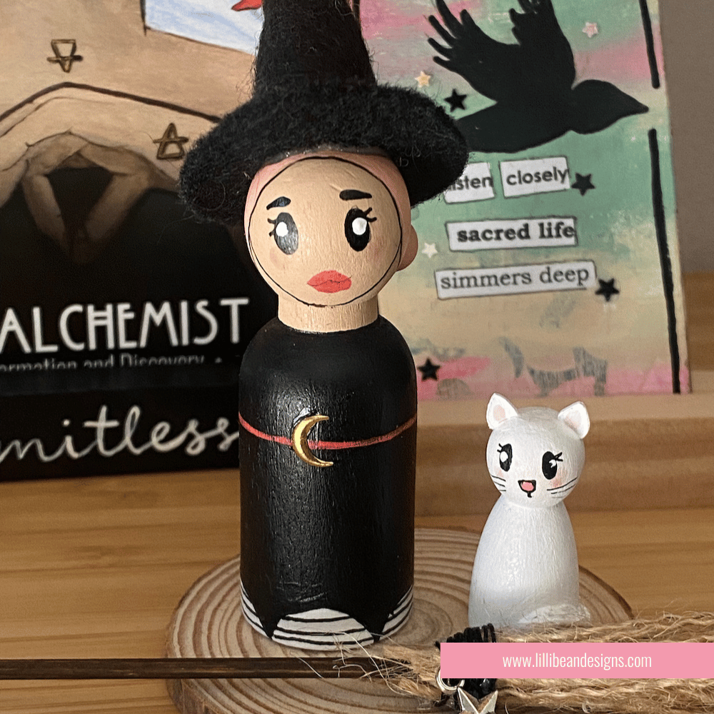 Wooden figurine of a witch and a cat on a wooden surface with a book in the background.