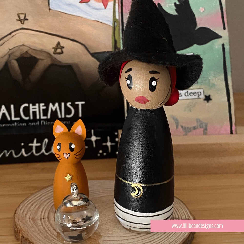 Wooden peg doll of a witch with a cat and lantern on a wooden surface, with 'Alchemist' and 'Mithli' branding in the background.