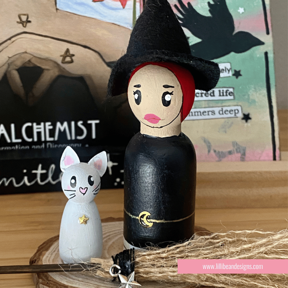 Wooden peg doll of a witch with a cat on a wooden surface with books in the background.